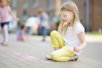 Cute little girl drawing with colorful chalks on a sidewalk. Summer activity for small kids. © MNStudio