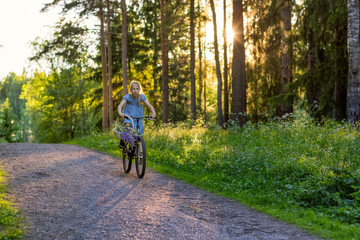 Fototapeta na wymiar Girl riding a bicycle in the woods with a basket of flowers, evening light