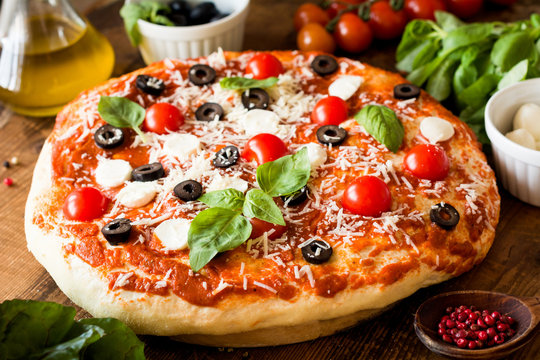 Pizza with tomatoes, mozzarella cheese, black olives and basil. Delicious italian pizza on wooden pizza board. Closeup view, selective focus