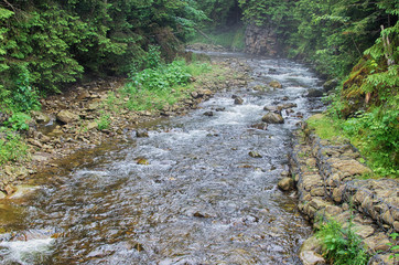 A stream in the mountains flows along the rocks and a stormy waterfall