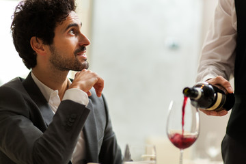Waiter pouring red wine to a man
