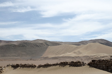Sand dunes of the desert and remains of stone walls covered with sand in front