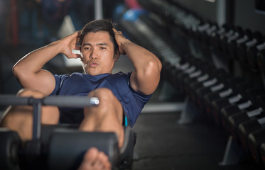 Asian man doing sit-ups at gym.