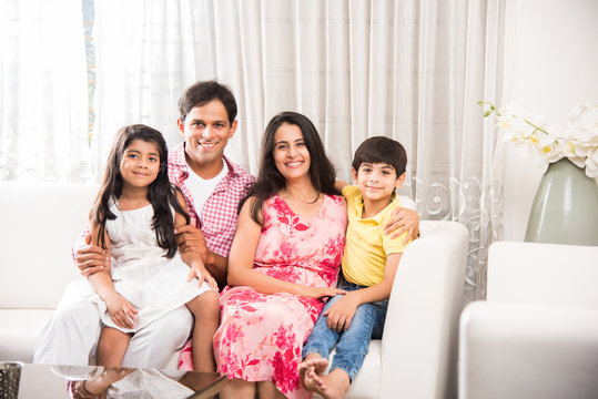 Candid Portrait Of Smart Indian Family Of Four While Sitting On Sofa. Indian Or Asian Family Group Photo. Selective Focus