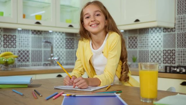 Close up portrait of cute young girl drawing the picture from the tablet at the kitchen, possing and smiling on camera.