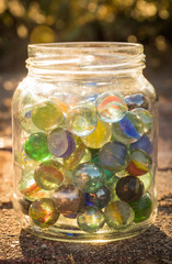 Glass jar full of marbles in the evening sun.
Old fashioned toys, literally put in the sun.
Warm glow through the glass and a choice of colors.