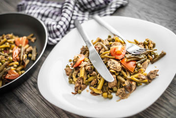 Plate with chicken meat and vegetable on wooden table.