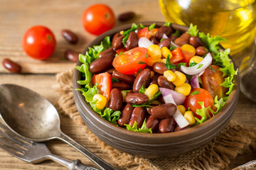 Fresh vegetable salad with beans in ceramic bowl on wooden table.