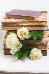 Old books pile with white rose flowers on white chair background