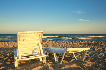 Two deckchairs on the beach with bright sun and waves