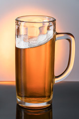 Large glass mug with a light beer covered with droplets on a mirror black surface