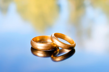Two bright golden wedding rings on abstract nature background