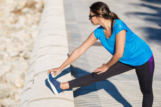 Young sportswoman stretching leg outside on sunny day