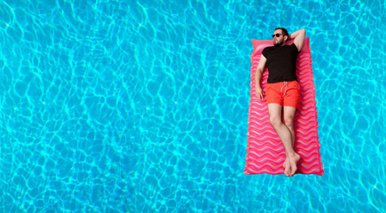 Man in t-shirt and shorts on inflatable mattress in the swimming pool.