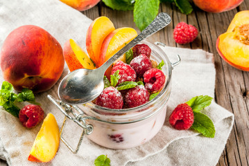 Summer healthy breakfast. Overnight oatmeal in a jar, granola, nuts, fresh raspberries and peach, decorated with mint leaves. On the old rustic wooden table. Copy space