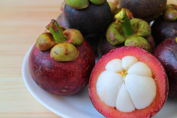 Ripe Purple Mangosteen Whole Fruits and Opened to Show tasty Pure White Meat on a Plate