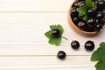black currant in wooden bowl with green leaf on white wooden background. top view