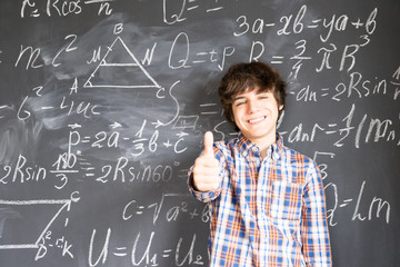 Teenage Boy showing thumb up finding idea with complicated math formulas on black board