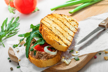 Toast sandwich with tuna, tomato, onion and arugula. Traditional healthy food made of fish, vegetables and grilled bread.