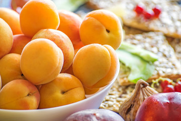 Naklejka na ściany i meble Fresh apricots in a white dish and other fruits on the kitchen table.Healthy lifestyle