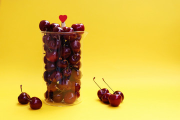 Fresh cherry berries in a glass jug isolated on a yellow background