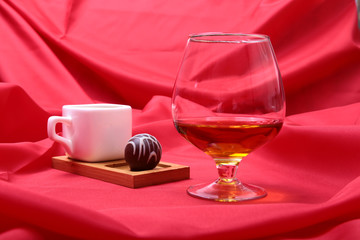 White cup of coffee and cognac in a glasses, pralines on red background.