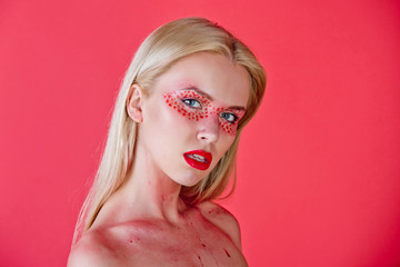 pretty blonde woman with creative fashionable makeup on red background