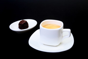 White cup of classic espresso coffee and pralines on black background.