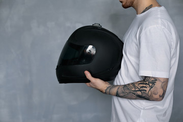 Cropped profile portrait of bearded Caucasian motorcyclist with tattooed arm holding black shiny...