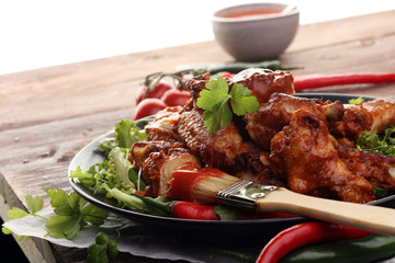 barbecue chicken wings close up on wooden tray with red spice sauce and salad