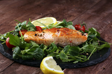 baked salmon grilled pepper lemon on a plate with lettuce leaves and tomato on wood background - healthy eating concept