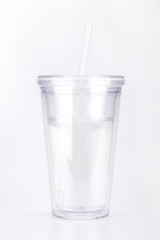 Clear plastic tumbler glass with lid and straw on a white surface. Travel cup isolated on white background.