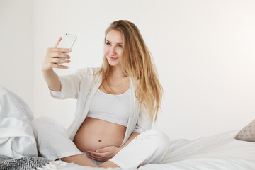 Prenatal selfie. Pregnant future mom making a self portrait using a smart phone smiling holding her belly