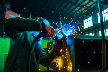 The worker in overalls and a protective mask welds metal with a welding machine. Profession welder....