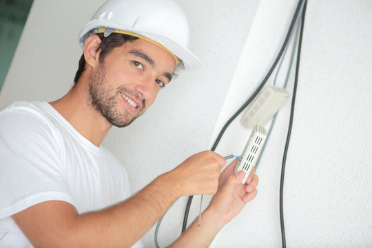 handsome electrician wiring to the wall at construction site