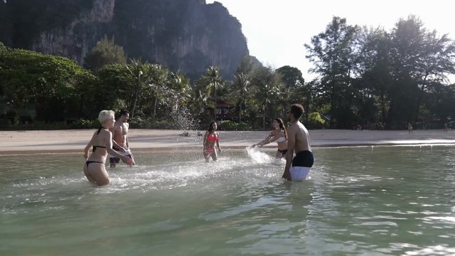 People Splashing In Water, Cheerful Young Man And Woman Group Having Fun On Beach In Mountains Slow Motion 120