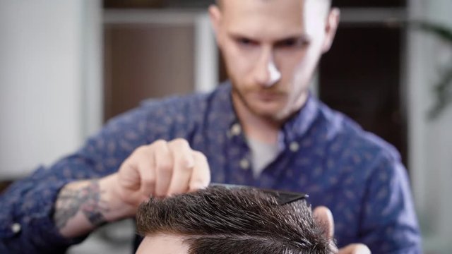 close up shot of the head of a man who combs his hair and makes a fashionable styling in barbershop with a comb and a hair gel