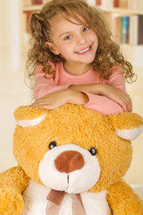 A portrait of a young pretty girl smiling and posing over her teddy bear s head in a doctor office background