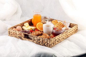 breakfast in bed with fruits and pastries on a tray -waffles, croissants, coffe and juice