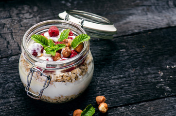 Full jar of muesli, yogurt, raspberries, nuts on a black, burnt wood table. Homemade breakfast cereals food. Healthy eating