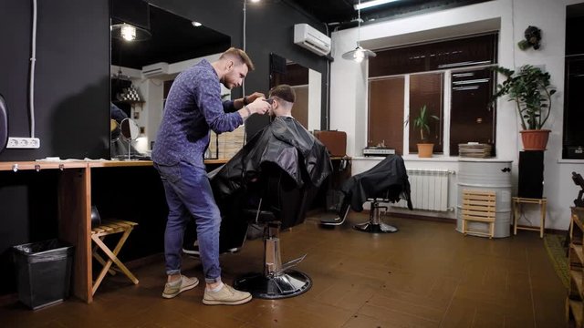 An adult hairdresser in stylish clothes shaves the head of a man, a stylist creates a fashionable hairstyle with the help of a shaver in a hair salon