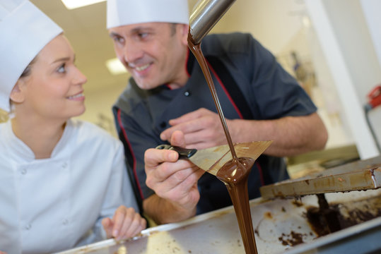 smiling chef and assistant melting chocolate at bakery