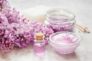 Fototapeta na wymiar organic salt, cream, extract in lilac cosmetic set with flowers on stone table background