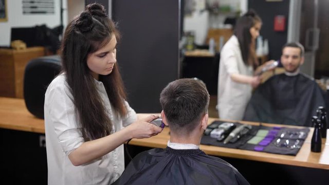 The hair stylist chooses the lower part of the hair on the head in order to create a stylish hairstyle at the beauty salon for men, the visitor looks in the mirror