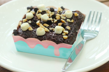 Brownie chocolate cake have marshmallow, almond, chocolate- chip on topping and have fork beside on white dish