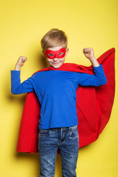 Boy in red super hero cape and mask. Superman. Studio portrait over yellow background