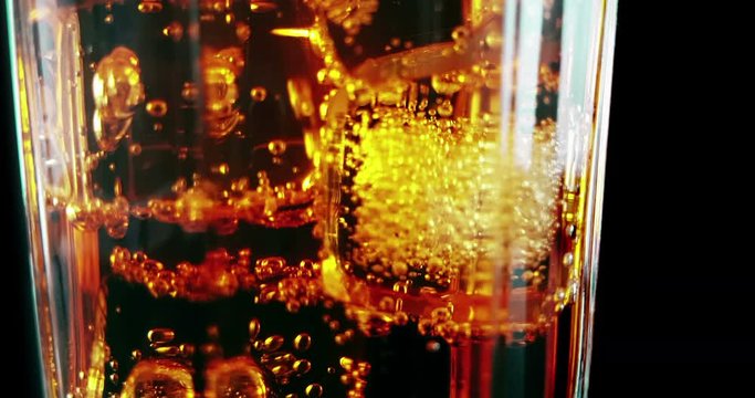 close-up of drinking glass of spritz aperitif aperol orange cocktail with ice cubes, with fizzy bubbles movement on black background, holiday and summer time concept