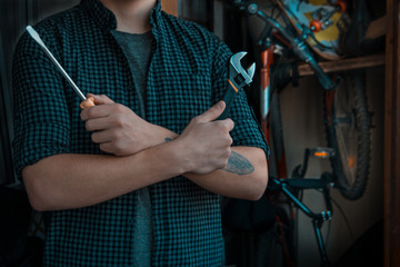 Cool classy young dude with a tattoo preparing to fix his bicycle with tools before taking a ride - obrazy, fototapety, plakaty