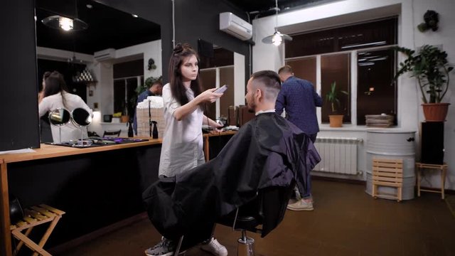 A young woman stylist by the hair trimmed bangs with a trimmer for the visitor barbershop, clients of the beauty salon expects to get a new hairstyle