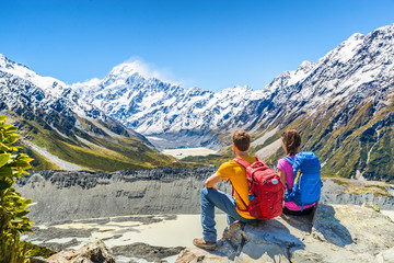 Fototapeta premium Backpackers couple hiking looking at Mount Cook view on mountains tramping in New Zealand. People hikers relaxing during hike in alps of south island.